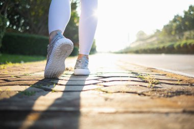 Spor kıyafeti giyen ve spor ayakkabısı giyen genç bir kadın gideceği yere giden yolda yürüyor. Genç bir kadın iki ayağıyla hedefine doğru kararlı bir şekilde yürüyor..