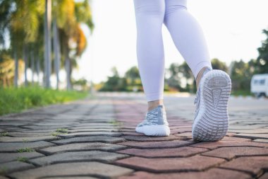 Spor kıyafeti giyen ve spor ayakkabısı giyen genç bir kadın gideceği yere giden yolda yürüyor. Genç bir kadın iki ayağıyla hedefine doğru kararlı bir şekilde yürüyor..