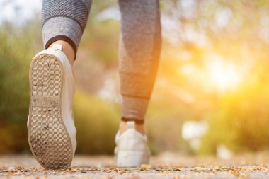 Spor kıyafeti giyen ve spor ayakkabısı giyen genç bir kadın gideceği yere giden yolda yürüyor. Genç bir kadın iki ayağıyla hedefine doğru kararlı bir şekilde yürüyor..