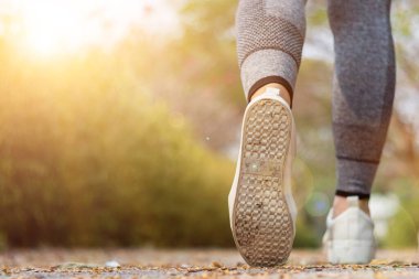 Spor kıyafeti giyen ve spor ayakkabısı giyen genç bir kadın gideceği yere giden yolda yürüyor. Genç bir kadın iki ayağıyla hedefine doğru kararlı bir şekilde yürüyor..