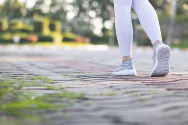 Spor kıyafeti giyen ve spor ayakkabısı giyen genç bir kadın gideceği yere giden yolda yürüyor. Genç bir kadın iki ayağıyla hedefine doğru kararlı bir şekilde yürüyor..