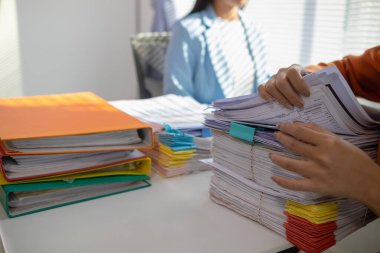 İki iş kadını, daha önce imzalanan belgelerin orijinalliğini doğrulamak için masadaki bir yığın belgeyi incelemek üzere birlikte çalışıyorlar..