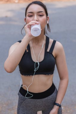 Plastik şişeden su içen güzel bir Asyalı koşucunun portresi. Çünkü koşmaktan yorgun hissediyor ve mola için su içmek istiyor. Güzel Asyalı kadın yorulduktan sonra su içiyor.