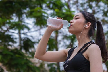 Plastik şişeden su içen güzel bir Asyalı koşucunun portresi. Çünkü koşmaktan yorgun hissediyor ve mola için su içmek istiyor. Güzel Asyalı kadın yorulduktan sonra su içiyor.