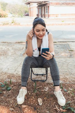 Sıkı spor giyimli Asyalı güzel koşucu tek başına ayakta duruyor ve moladan sonra müzik dinlemek için telefonunu açık tutuyor. Telefonunu tutan güzel kadınlar şarkıları seçer koşarken dinlerler