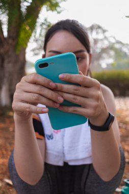 Sıkı spor giyimli Asyalı güzel koşucu tek başına ayakta duruyor ve moladan sonra müzik dinlemek için telefonunu açık tutuyor. Telefonunu tutan güzel kadınlar şarkıları seçer koşarken dinlerler