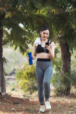 Sıkı spor giyimli Asyalı güzel koşucu tek başına ayakta duruyor ve moladan sonra müzik dinlemek için telefonunu açık tutuyor. Telefonunu tutan güzel kadınlar şarkıları seçer koşarken dinlerler