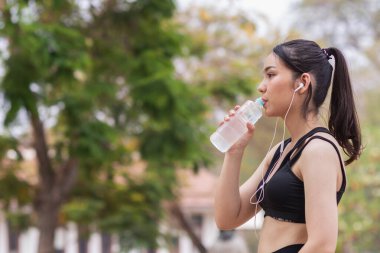Plastik şişeden su içen güzel bir Asyalı koşucunun portresi. Çünkü koşmaktan yorgun hissediyor ve mola için su içmek istiyor. Güzel Asyalı kadın yorulduktan sonra su içiyor.