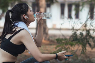 Plastik şişeden su içen güzel bir Asyalı koşucunun portresi. Çünkü koşmaktan yorgun hissediyor ve mola için su içmek istiyor. Güzel Asyalı kadın yorulduktan sonra su içiyor.