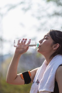 Plastik şişeden su içen güzel bir Asyalı koşucunun portresi. Çünkü koşmaktan yorgun hissediyor ve mola için su içmek istiyor. Güzel Asyalı kadın yorulduktan sonra su içiyor.