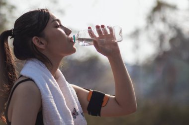Plastik şişeden su içen güzel bir Asyalı koşucunun portresi. Çünkü koşmaktan yorgun hissediyor ve mola için su içmek istiyor. Güzel Asyalı kadın yorulduktan sonra su içiyor.