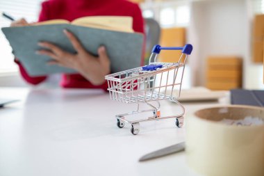 Kırmızı gömlekli Asyalı iş kadını ürün siparişlerini kontrol ediyor ve çevrimiçi alışveriş uygulamalarına giren siparişlere göre müşterilere yetecek kadar hisse senedi hesaplıyor. Mesaj için Boşluğu Kopyala