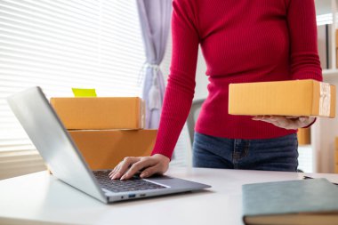 Kırmızı tişörtlü bir iş kadını elinde bir online alışveriş uygulaması aracılığıyla ürün sipariş eden müşteriye teslim etmeye hazır bir paket kutusu tutuyor. Uygulama yoluyla çevrimiçi bir mağaza açma kavramını kabul et