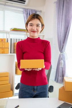 Kırmızı tişörtlü bir iş kadını elinde bir online alışveriş uygulaması aracılığıyla ürün sipariş eden müşteriye teslim etmeye hazır bir paket kutusu tutuyor. Uygulama yoluyla çevrimiçi bir mağaza açma kavramını kabul et