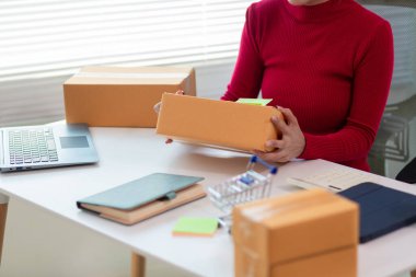 Kırmızı tişörtlü bir iş kadını elinde bir online alışveriş uygulaması aracılığıyla ürün sipariş eden müşteriye teslim etmeye hazır bir paket kutusu tutuyor. Uygulama yoluyla çevrimiçi bir mağaza açma kavramını kabul et