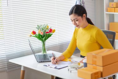 Asyalı işkadını, çevrimiçi alışveriş başvurusundan gelen siparişe göre ürünleri doğru şekilde teslim etmek için stok ve siparişleri kontrol ediyor. Asyalı iş kadını çevrimiçi alışveriş işine yatırım yapmaktan mutluluk duyar