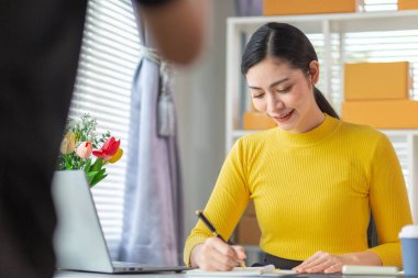 Asyalı işkadını, çevrimiçi alışveriş başvurusundan gelen siparişe göre ürünleri doğru şekilde teslim etmek için stok ve siparişleri kontrol ediyor. Asyalı iş kadını çevrimiçi alışveriş işine yatırım yapmaktan mutluluk duyar