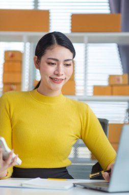 Asyalı işkadını, çevrimiçi alışveriş başvurusundan gelen siparişe göre ürünleri doğru şekilde teslim etmek için stok ve siparişleri kontrol ediyor. Asyalı iş kadını çevrimiçi alışveriş işine yatırım yapmaktan mutluluk duyar