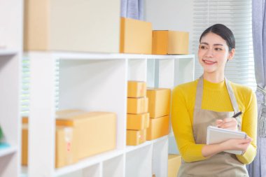 Bir iş kadını, siparişleri göndermeden önce evindeki ürünleri dağıtmak ve siparişleri kontrol etmek için internet üzerinden satış işine yatırım yapar..