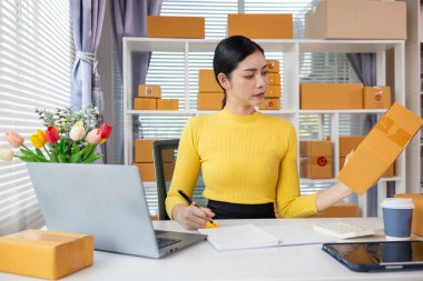 Asyalı işkadını siparişleri ve müşterilerin siparişlerini kontrol ediyor ve siparişleri online alışveriş uygulaması yoluyla teslim ediyor. Uygulama yoluyla çevrimiçi iş fikri