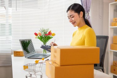 Asyalı işkadını siparişleri ve müşterilerin siparişlerini kontrol ediyor ve siparişleri online alışveriş uygulaması yoluyla teslim ediyor. Uygulama yoluyla çevrimiçi iş fikri