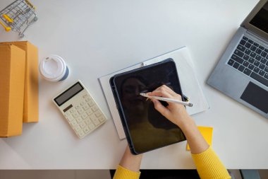 Asyalı işkadını, çevrimiçi alışveriş başvurusundan gelen siparişe göre ürünleri doğru şekilde teslim etmek için stok ve siparişleri kontrol ediyor. Asyalı iş kadını çevrimiçi alışveriş işine yatırım yapmaktan mutluluk duyar