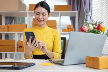 İş kadını, müşterilerden sipariş almak için cep telefonu uygulaması üzerinden ev ofisi kurar ve müşterilerle iletişime geçmek ve siparişleri göndermeden önce onaylamak için cep telefonunu kullanır. Boşluğu kopyala