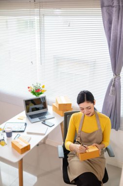 Asyalı işkadını, çevrimiçi alışveriş başvurusundan gelen siparişe göre ürünleri doğru şekilde teslim etmek için stok ve siparişleri kontrol ediyor. Asyalı iş kadını çevrimiçi alışveriş işine yatırım yapmaktan mutluluk duyar