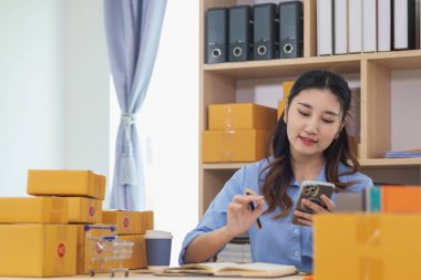 Asyalı kadın evini ofis olarak kullanarak küçük bir KOBİ işine başladı. Paketlemeden ve müşterilere göndermeden önce ürünleri Düzen 'e göre onaylamak için müşterileri arıyor. Boşluğu Kopyala