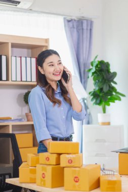 Asyalı kadın evini ofis olarak kullanarak küçük bir KOBİ işine başladı. Paketlemeden ve müşterilere göndermeden önce ürünleri Düzen 'e göre onaylamak için müşterileri arıyor. Boşluğu Kopyala