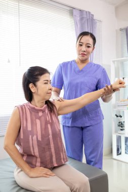 Kadın doktor yaşlı bir insana bakıyor ve yaşlı bir insanın fiziksel terapi görmesine, kasların çalışmasına ve kas sisteminin işlevlerini kontrol etmesine yardım ediyor..