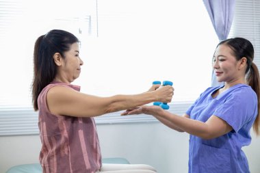 Kadın doktor yaşlı bir insana bakıyor ve yaşlı bir insanın fiziksel terapi görmesine, kasların çalışmasına ve kas sisteminin işlevlerini kontrol etmesine yardım ediyor..