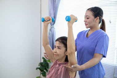 Kadın doktor yaşlı bir insana bakıyor ve yaşlı bir insanın fiziksel terapi görmesine, kasların çalışmasına ve kas sisteminin işlevlerini kontrol etmesine yardım ediyor..