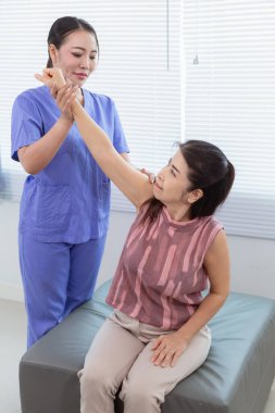 Kadın doktor yaşlı bir insana bakıyor ve yaşlı bir insanın fiziksel terapi görmesine, kasların çalışmasına ve kas sisteminin işlevlerini kontrol etmesine yardım ediyor..