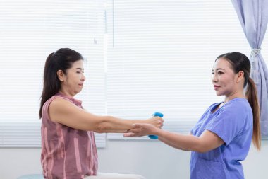 Kadın doktor yaşlı bir insana bakıyor ve yaşlı bir insanın fiziksel terapi görmesine, kasların çalışmasına ve kas sisteminin işlevlerini kontrol etmesine yardım ediyor..