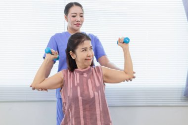 Kadın doktor yaşlı bir insana bakıyor ve yaşlı bir insanın fiziksel terapi görmesine, kasların çalışmasına ve kas sisteminin işlevlerini kontrol etmesine yardım ediyor..