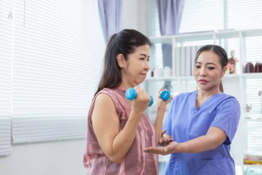 Kadın doktor yaşlı bir insana bakıyor ve yaşlı bir insanın fiziksel terapi görmesine, kasların çalışmasına ve kas sisteminin işlevlerini kontrol etmesine yardım ediyor..