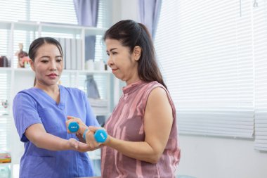 Kadın doktor yaşlı bir insana bakıyor ve yaşlı bir insanın fiziksel terapi görmesine, kasların çalışmasına ve kas sisteminin işlevlerini kontrol etmesine yardım ediyor..