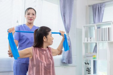 Kadın doktor yaşlı bir insana bakıyor ve yaşlı bir insanın fiziksel terapi görmesine, kasların çalışmasına ve kas sisteminin işlevlerini kontrol etmesine yardım ediyor..