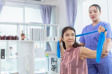 Kadın doktor yaşlı bir insana bakıyor ve yaşlı bir insanın fiziksel terapi görmesine, kasların çalışmasına ve kas sisteminin işlevlerini kontrol etmesine yardım ediyor..
