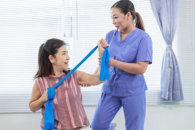 Kadın doktor yaşlı bir insana bakıyor ve yaşlı bir insanın fiziksel terapi görmesine, kasların çalışmasına ve kas sisteminin işlevlerini kontrol etmesine yardım ediyor..