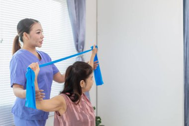 Kadın doktor yaşlı bir insana bakıyor ve yaşlı bir insanın fiziksel terapi görmesine, kasların çalışmasına ve kas sisteminin işlevlerini kontrol etmesine yardım ediyor..