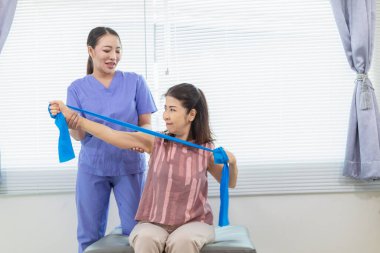 Kadın doktor yaşlı bir insana bakıyor ve yaşlı bir insanın fiziksel terapi görmesine, kasların çalışmasına ve kas sisteminin işlevlerini kontrol etmesine yardım ediyor..