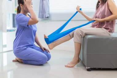 Kadın doktor yaşlı bir insana bakıyor ve yaşlı bir insanın fiziksel terapi görmesine, kasların çalışmasına ve kas sisteminin işlevlerini kontrol etmesine yardım ediyor..