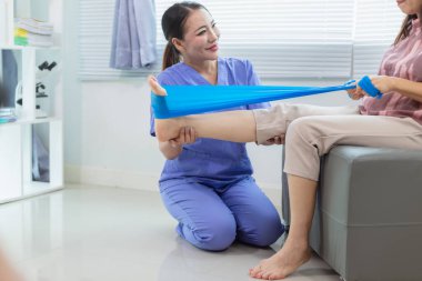 Kadın doktor yaşlı bir insana bakıyor ve yaşlı bir insanın fiziksel terapi görmesine, kasların çalışmasına ve kas sisteminin işlevlerini kontrol etmesine yardım ediyor..