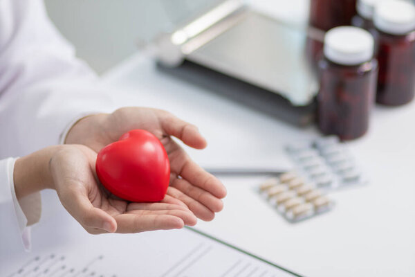 кардиолог держит в руке красный символ сердца, чтобы продемонстрировать уход и лечение сердечных заболеваний. Женщина-врач держит в руках символ красного сердца, символизирующий уход и лечение сердечных заболеваний. Копировальное пространство