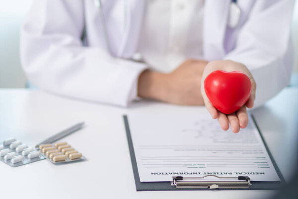 кардиолог держит в руке красный символ сердца, чтобы продемонстрировать уход и лечение сердечных заболеваний. Женщина-врач держит в руках символ красного сердца, символизирующий уход и лечение сердечных заболеваний. Копировальное пространство