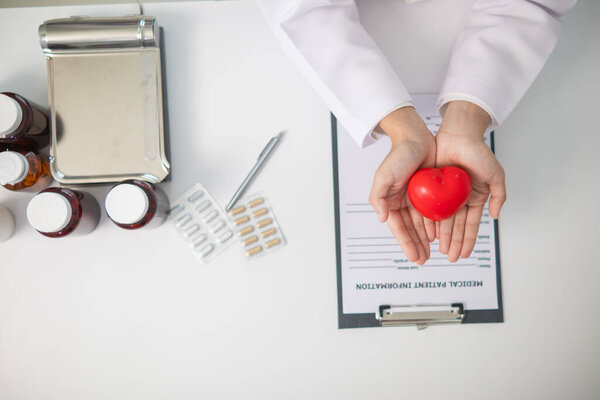 кардиолог держит в руке красный символ сердца, чтобы продемонстрировать уход и лечение сердечных заболеваний. Женщина-врач держит в руках символ красного сердца, символизирующий уход и лечение сердечных заболеваний. Вид сверху