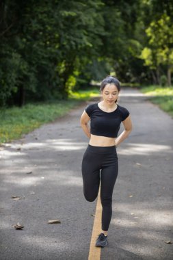 Spor kıyafetleri giyen ve vücudunu ısıtan güzel bayan koşucunun portresi. Sabah koşuya hazır ol. Sağlığına dikkat et. Kadın koşucu tek başına vücudunu ısıtır parkta koşuya hazırlanır..