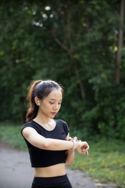 Bileğindeki akıllı saate bakan bir koşucunun portresi kalp atışlarını ve koşu mesafesini kontrol ediyor. Koşucu dikkat ediyor. Akıllı saati bileğinde. Nabzını ve koşu mesafesini kontrol ediyor..